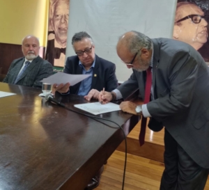 Da esq. para a dir., sentados, Carlos Alberto Vilhena e Octávio Costa; de pé, Armando de Souza assinando o Memorando de Entendimento